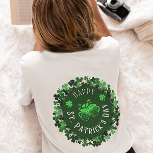 Könnte beinhalten: Weißes T-Shirt mit einem St. Patrick's Day-Design. Das Design zeigt einen grünen Kreis mit dem Text "Happy St. Patrick's Day" und zwei grüne Bierkrüge. Das Design ist von grünen Kleeblättern umgeben.