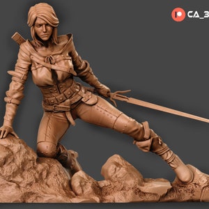 May include: A brown clay sculpture of a female figure in a fantasy warrior pose, holding a sword and standing on a rocky base.