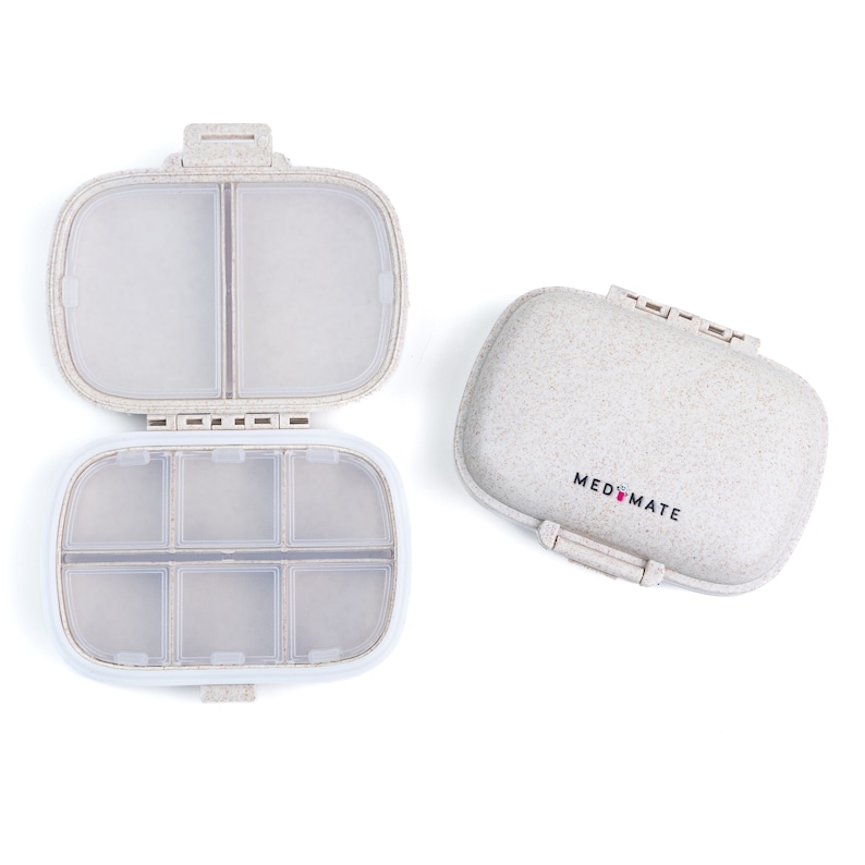 Puede incluir: Un pastillero beige con superficie texturizada, abierto para revelar seis compartimentos. La tapa cerrada muestra el texto "MED MATE" en negro. El pastillero est&aacute; dise&ntilde;ado para almacenar y organizar medicamentos.