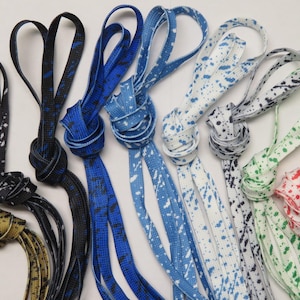 May include: A collection of colorful, patterned face mask lanyards. The lanyards are in various colors, including black, blue, white, green, and red, with a speckled design. Each lanyard is knotted at the center and has loops at the ends.