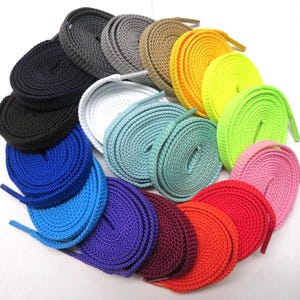 May include: A collection of flat, woven shoelaces arranged in a circular pattern, featuring a wide variety of colors including black, gray, tan, yellow, neon green, white, light blue, teal, purple, maroon, orange, red, and pink.
