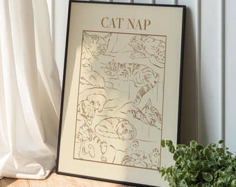 May include: A black framed print with the title "CAT NAP" in gold lettering. The print features a line drawing of multiple cats sleeping in various positions.