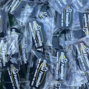 May include: A collection of black and yellow Global Formulas keychains in clear plastic packaging. Each keychain has the text "Global Formulas" and "Train Hard. Demand the Best."