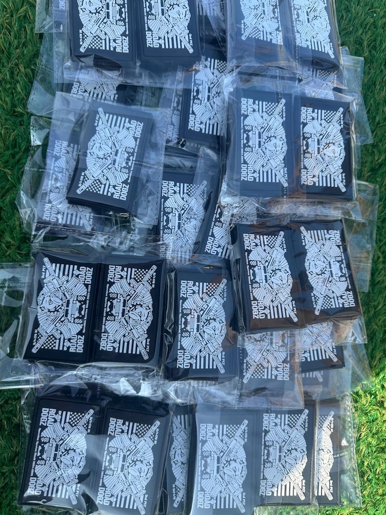 May include: A collection of black rectangular patches, each individually packaged in clear plastic. The patches feature a detailed white graphic design with the text "ROAD DOGZ 2800" and other text. The patches are arranged on a green surface.
