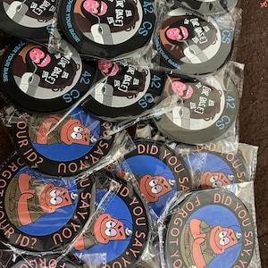 May include: A collection of round black coasters with various designs. Some feature a cartoon face with a computer mouse and the text "COMM ALL OVER YOUR BASE" and "42 CS [UR BASE]". Others display a cartoon character with the text "DID YOU SAY, YOU FORGOT YOUR ID?"