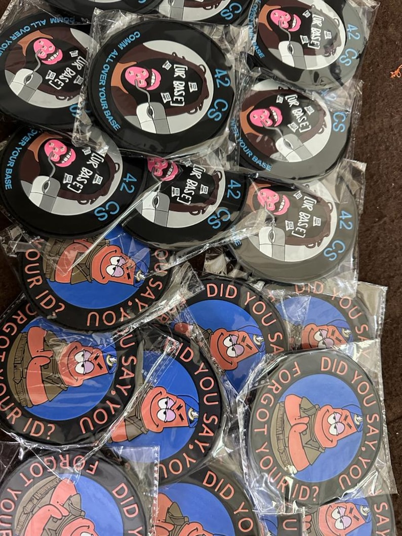 May include: A collection of round black coasters with various designs. Some feature a cartoon face with a computer mouse and the text "COMM ALL OVER YOUR BASE" and "42 CS [UR BASE]". Others display a cartoon character with the text "DID YOU SAY, YOU FORGOT YOUR ID?"