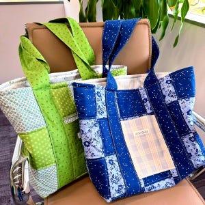 May include: Two patchwork tote bags. One is green with floral and polka dot patterns, the other is blue with floral and polka dot patterns. Both have matching straps and a pocket with text. The bags are sitting on a chair.