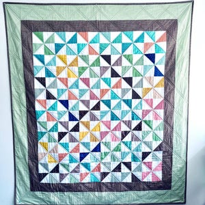 Puede incluir: Un edredón colorido con un diseño geométrico. El edredón presenta un patrón de triángulos en varios colores, incluyendo azul, verde, rosa y amarillo. Tiene un borde marrón oscuro y un borde de cuadros verdes y blancos.