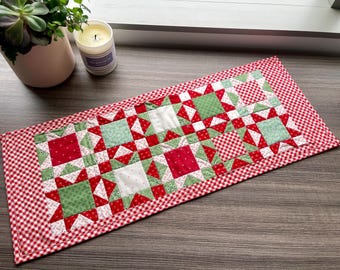 May include: A red and green patchwork table runner with a gingham border. The runner is made of squares of fabric in different patterns and colours.