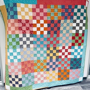 May include: A colorful patchwork quilt with a vibrant mix of patterns and colors, including red, blue, green, yellow, and white. The quilt features a grid-like design with squares of various fabrics, creating a cozy and visually appealing textile.