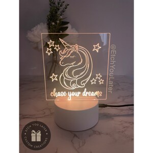 May include: A white acrylic night light with a unicorn design and the text "chase your dreams". The light is illuminated and has a white base. The text "@EtchYouLater" is on the side of the light.