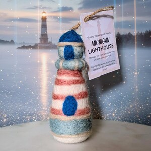 May include: A handcrafted lighthouse ornament with a blue and white striped design, featuring a blue top and a blue oval detail. The ornament has a tag that reads "MICHIGAN LIGHTHOUSE".