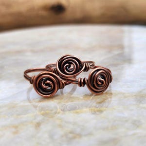 May include: Three copper wire rings with a spiral design. The rings are stacked on top of each other.