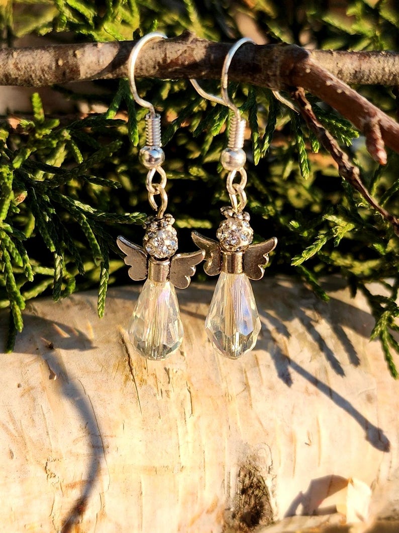 May include: Silver angel dangle earrings with clear crystal teardrop charms. The angels have rhinestone accents.