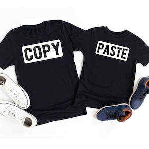 May include: Two black t-shirts with white text. One shirt says "COPY" and the other says "PASTE".