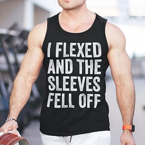 May include: A black sleeveless shirt with the text "I Flexed And The Sleeves Fell Off" printed in white. The shirt is being worn by a person in a gym setting.