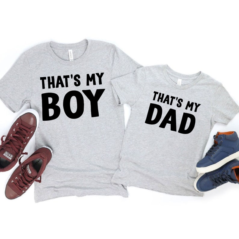 May include: Two gray t-shirts with black text. The larger shirt says "That's My Boy" and the smaller shirt says "That's My Dad".
