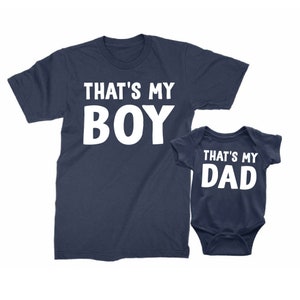 May include: A navy blue t-shirt with the text "That's My Boy" in white, and a navy blue baby bodysuit with the text "That's My Dad" in white.