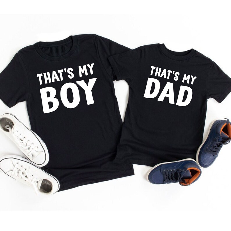 May include: Two black t-shirts with white text. One shirt says "That's My Boy" and the other says "That's My Dad".