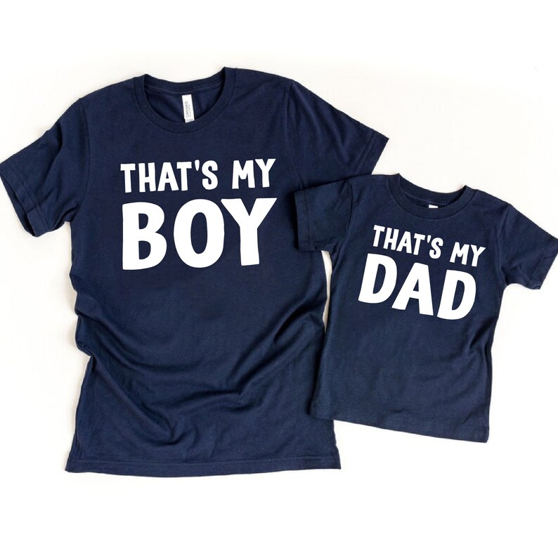 May include: Two navy blue t-shirts with white text. The larger shirt says "That's My Boy" and the smaller shirt says "That's My Dad".