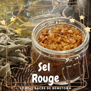 Puede incluir: Un tarro de cristal lleno de sal gruesa de color marrón rojizo, etiquetado como "Sel Rouge". El tarro tiene un cierre metálico y está sobre una superficie estampada. Salvia seca y pequeños recipientes de vidrio en el fondo, con detalles de estrellas doradas.