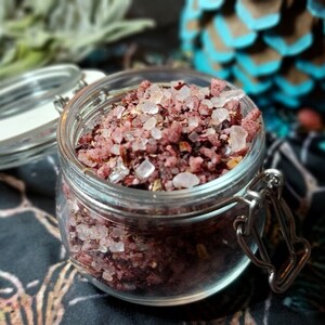 May include: A glass jar filled with pink bath salts, with a white lid and a silver clasp. The salts are a mixture of pink Himalayan salt and dried rose petals.