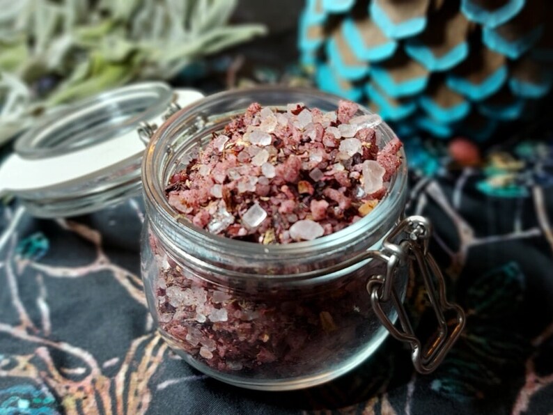 May include: A glass jar filled with pink bath salts, with a white lid and a silver clasp. The salts are a mixture of pink Himalayan salt and dried rose petals.