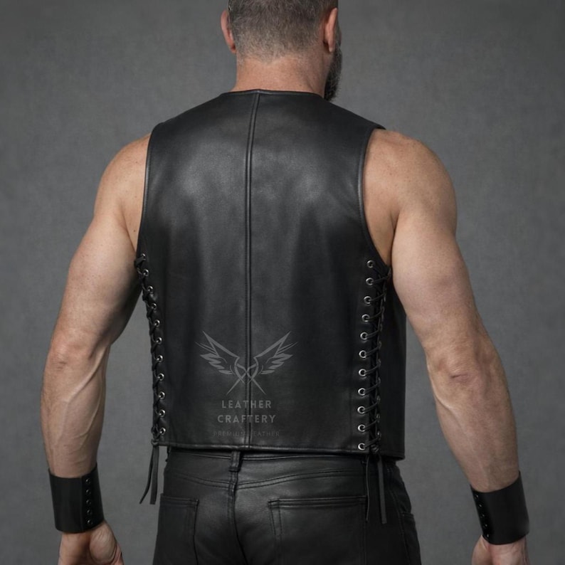May include: Black leather vest with lace-up sides. The vest has a sleeveless design and a round neckline. The back of the vest features a logo with the text "LEATHER CRAFTERY". The model is wearing black leather pants and a black wristband.