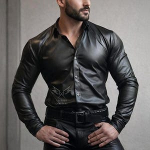 Op de afbeelding: Zwart leren overhemd met lange mouwen en een klassieke kraag. Het overhemd is dichtgeknoopt en wordt gedragen met een zwarte leren broek en een riem. De tekst "LEATHER CRAFTERY" is zichtbaar.