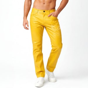 Può includere: Pantaloni in pelle giallo senape con vestibilità dritta. I pantaloni hanno un classico design a cinque tasche e un logo bianco sulla gamba destra. Il modello indossa scarpe da ginnastica bianche.