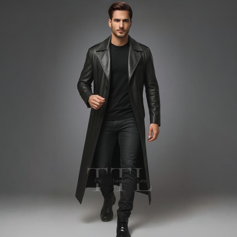 May include: A long, black leather trench coat with a classic design. The coat features a notched collar, a button-down front, and a long, flowing silhouette. The model is wearing a black shirt and black jeans.