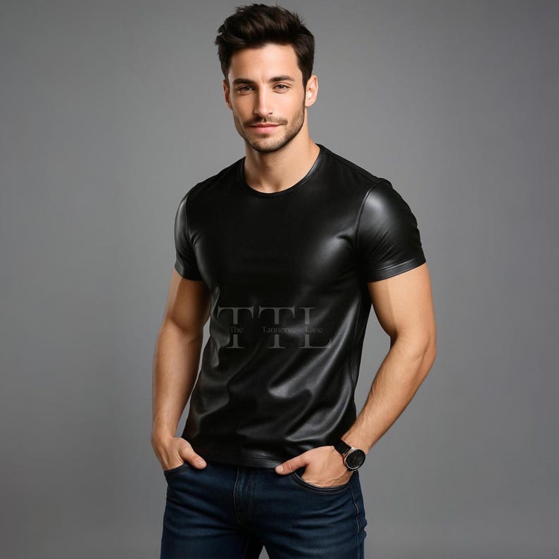 Puede incluir: Camiseta negra de manga corta con cuello redondo. La camiseta tiene un aspecto brillante, similar al cuero. El texto "TTL The Tanner Lane" est&aacute; impreso en la parte delantera. La persona lleva un reloj negro y vaqueros azules.