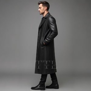 May include: A long, black leather coat with a classic design. The coat features a notched collar, front pockets, and a long length, reaching the ankles. The coat is worn with black pants and shoes. The Tannery Lane logo is visible on the coat.