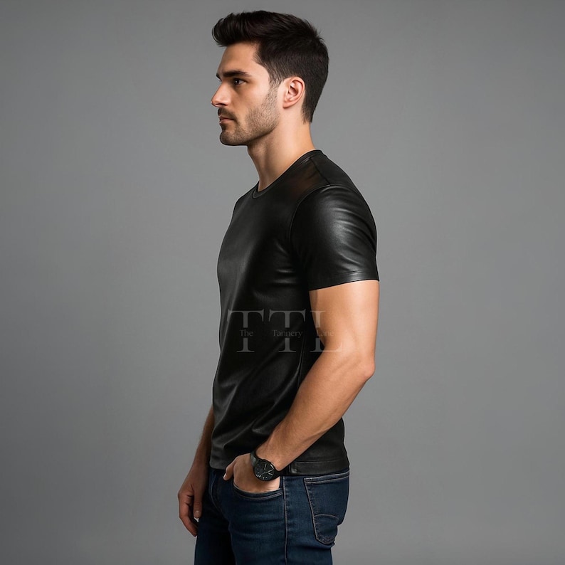 Puede incluir: Camiseta negra efecto cuero con mangas cortas y cuello redondo. La camiseta tiene un corte entallado. El modelo lleva vaqueros azules y un reloj negro. El logo TTI es visible en la camiseta.