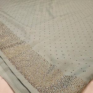 May include: A light blue fabric with a pattern of small gold sequins. The sequins are arranged in a repeating pattern, creating a subtle shimmer effect. The fabric is soft and smooth to the touch.