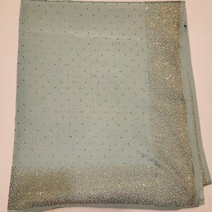 May include: A light blue scarf with a border of silver sequins. The scarf is made of a soft, silky material.