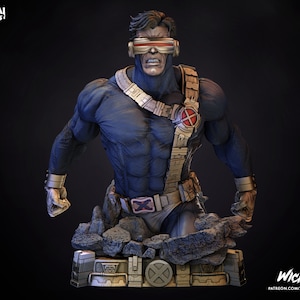 May include: A blue and gold bust of Cyclops, a superhero from the X-Men comics. He is wearing a blue and black costume with a red X on his chest. He has a red and silver visor over his eyes. The bust is set on a rocky base with a gold and silver base.