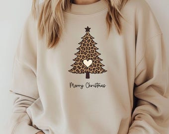 Könnte beinhalten: Ein beigefarbenes Sweatshirt mit Rundhalsausschnitt und einer Grafik eines Weihnachtsbaums mit braun-schwarzem Leopardenmuster, einem kleinen cremefarbenen Herz in der Mitte, einem dunklen Stern an der Spitze und dem Text Merry Christmas.