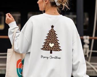 Könnte beinhalten: Ein weißes Langarm-Sweatshirt mit einer Grafik eines Weihnachtsbaums mit Leopardenmuster und einem kleinen cremefarbenen Herz in der Mitte. Der Text Merry Christmas ist in schwarzer Schreibschrift unter dem Baumdesign gedruckt.