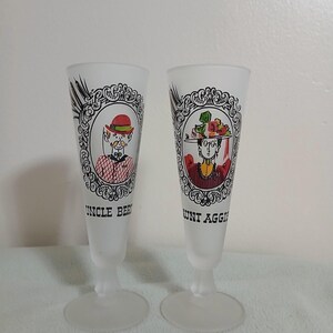 May include: Two frosted glass champagne flutes. Each flute features a decorative framed portrait of a person with the text "UNCLE BER" and "AUNT AGGI". The portraits are in color and the flutes have a wide base.