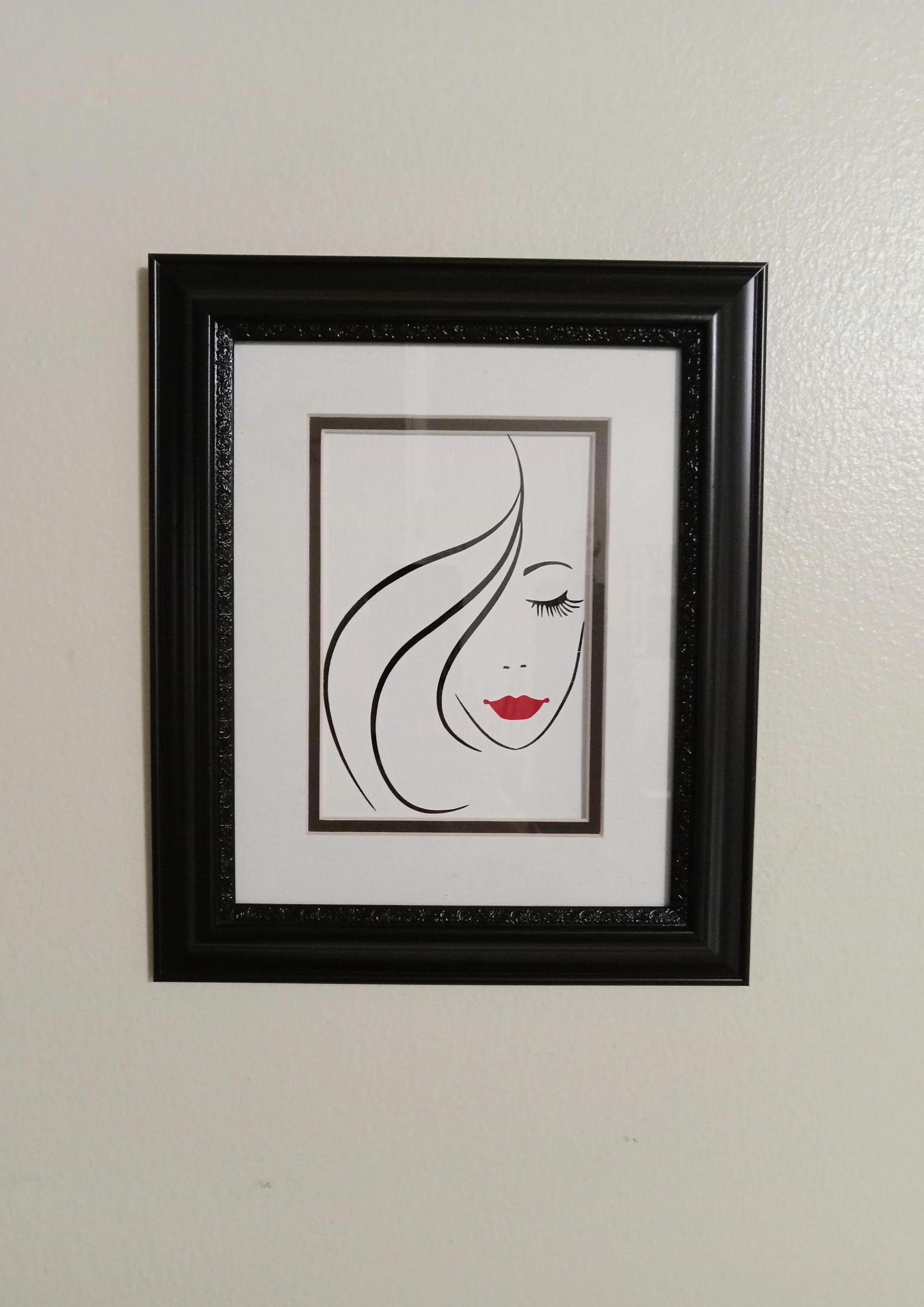 Imagen "Rostro de Mujer" sellada y paspartú en marco negro con diseño de pergamino. Cabello, rostro, nariz y ojos negros brillantes, con labios rojos brillantes.
