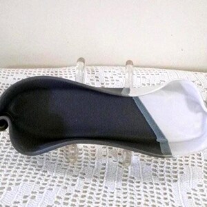 May include: A ceramic serving dish with a unique design. The dish is divided diagonally, with one side in matte black and the other in white. A thin, light blue stripe accents the division. The dish has a curved shape with a rolled edge.