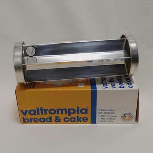 May include: A silver metal bread and cake mold with three different shapes: flower, heart, and star. The mold is on a yellow and blue box with the text "valtrompia bread & cake" printed on it.