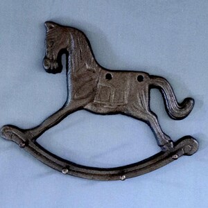 May include: A cast iron rocking horse wall decor in a dark bronze finish. The horse has a detailed mane, tail, and saddle. The rocker has three small holes for mounting. A charming accent for a nursery or child's room.