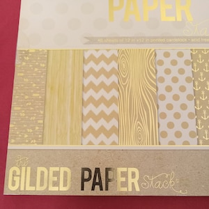 May include: A package of The Gilded Paper Stack, featuring 48 sheets of 12 in x 12 in printed cardstock. The paper has various designs, including arrows, wood grain, chevrons, polka dots, and anchors, all in gold on a neutral background.
