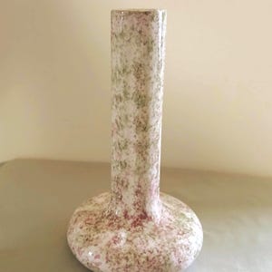May include: A ceramic bud vase with a cylindrical neck and a rounded base. The surface features a speckled, mottled pattern in shades of soft pink, sage green, and white, creating a textured appearance across the entire exterior of the vessel.
