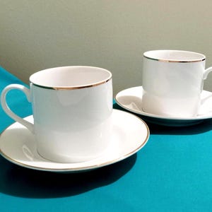 2~ 2000 Bob Mackie Design White Porcelain Trimmed In Gold, Flat Bottom Cups And Matching Saucers