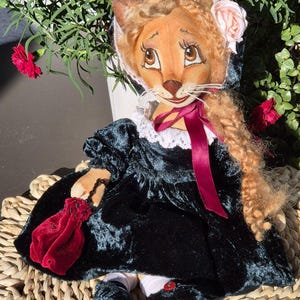 May include: A handmade doll with a lion-like face, wearing a dark green velvet dress with a white lace collar. The doll has a pink rose on its head and a red velvet pouch. The doll's hair is a light brown color, and it has a red ribbon.
