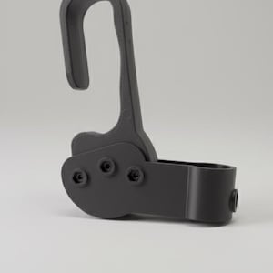 Może przedstawiać: Ciemnoszary, regulowany zacisk z zakrzywionym hakiem i cylindryczną podstawą. Zacisk ma trzy widoczne śruby i jest przeznaczony do mocowania do słupa lub pręta. Obiekt jest wykonany z matowego materiału.