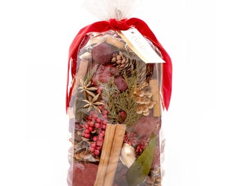 May include: A clear cellophane bag filled with potpourri, tied with a red ribbon. The potpourri includes cinnamon sticks, pine cones, star anise, and red berries. A tag is attached to the ribbon.